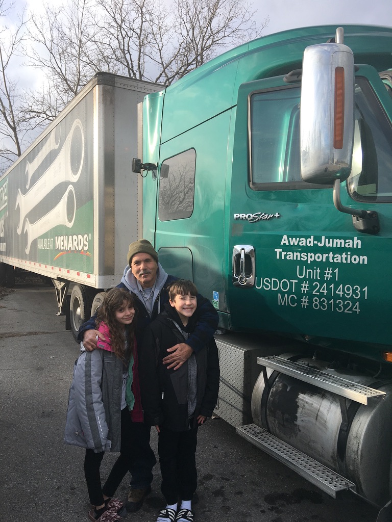 Zach’s dad, younger brother, and younger sister beside a green semi truck